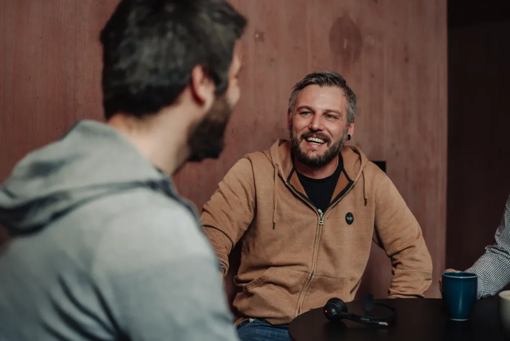 Zwei Mitarbeiter sitzen sich bei einem Kaffee gegenüber und lächeln sich an