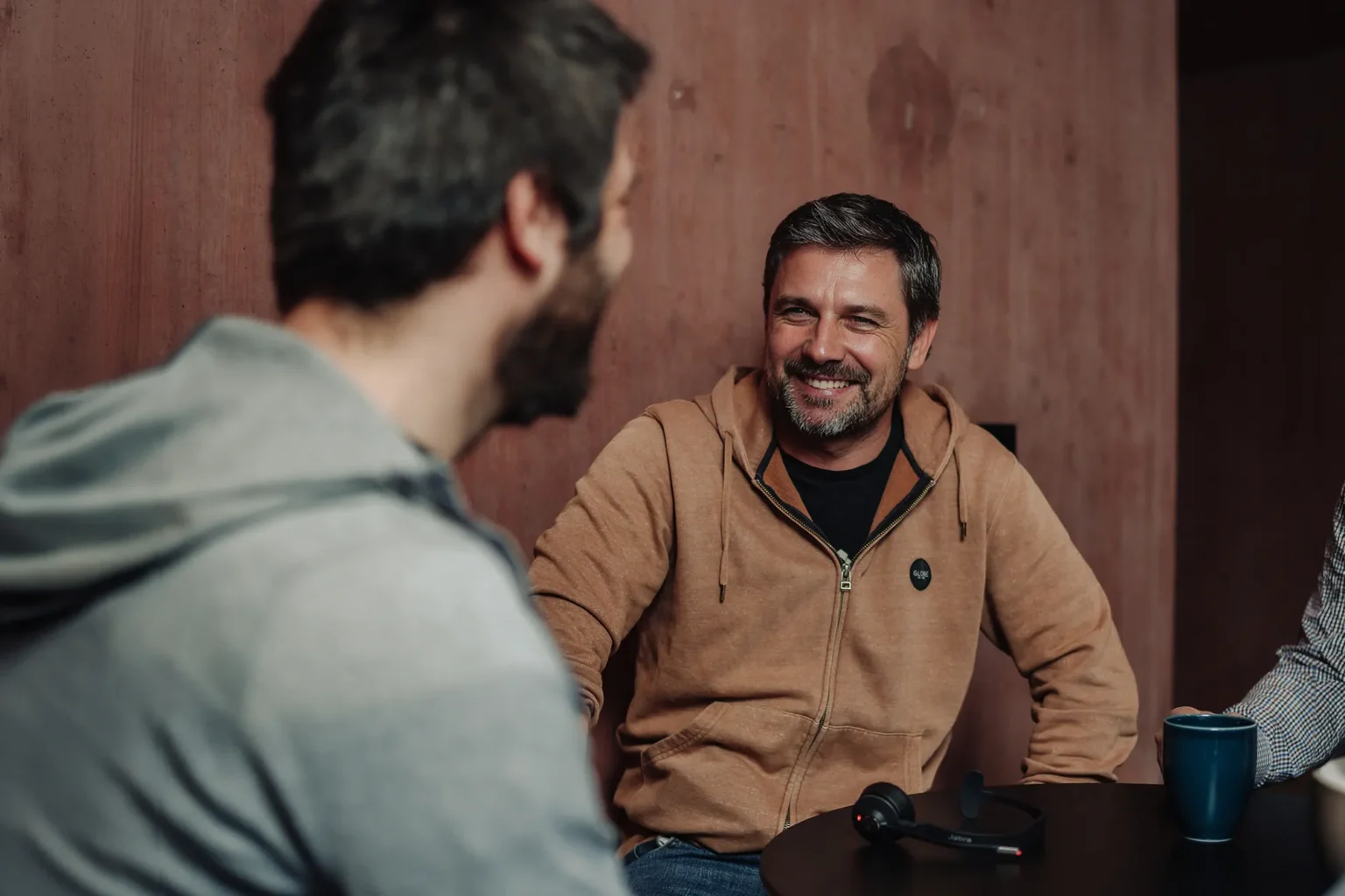 Zwei Mitarbeiter sitzen sich bei einem Kaffee gegenüber und lächeln sich an